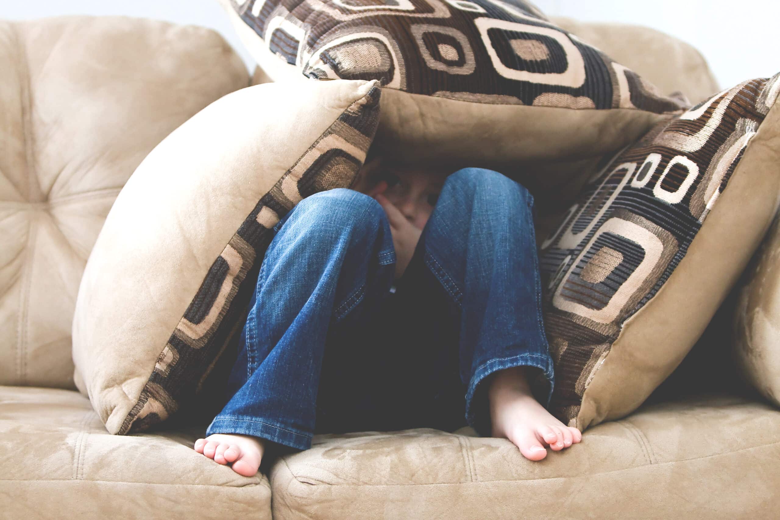 Lapsi piileskelee surullisen näköisenä sohvatyynyjen alla