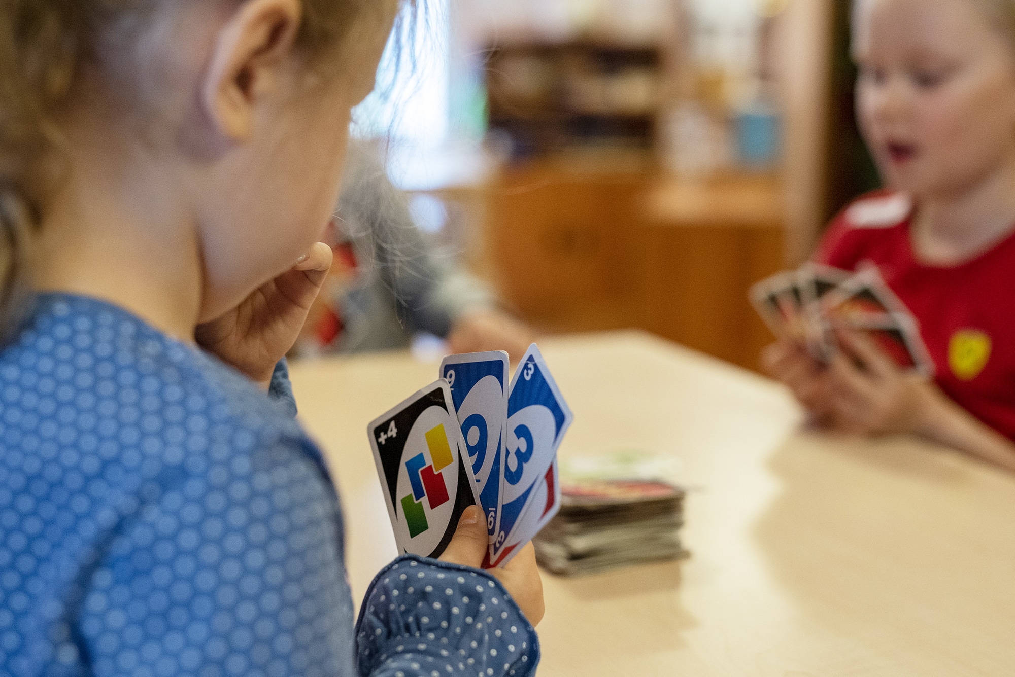 Kolme päiväkoti-ikäistä lasta istumassa pöydän ääressä pelaamassa Uno-korttipeliä.